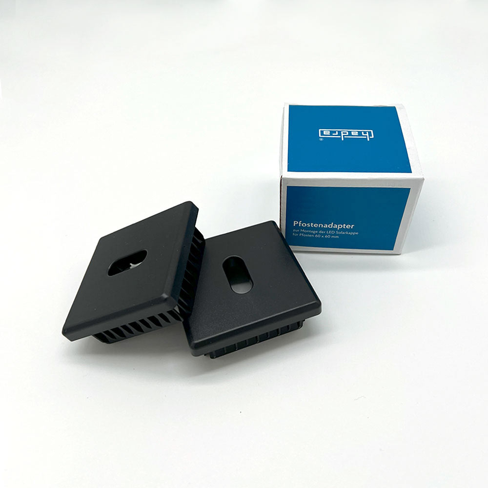 zwei schwarze Pfostenadapter 60x60 liegen leicht aufeinander fotografiert neben der blaueb Kartonverpackung von Hadra